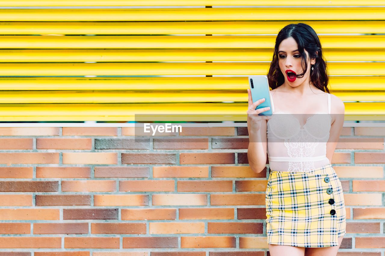 YOUNG WOMAN STANDING AGAINST YELLOW WALL