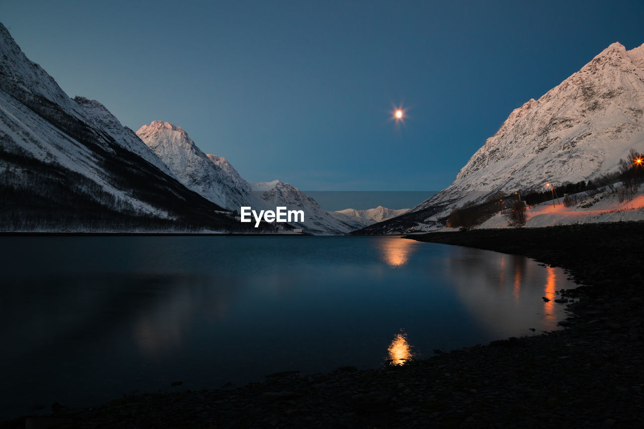 Scenic view of lake and snowcapped mountains against sky at night