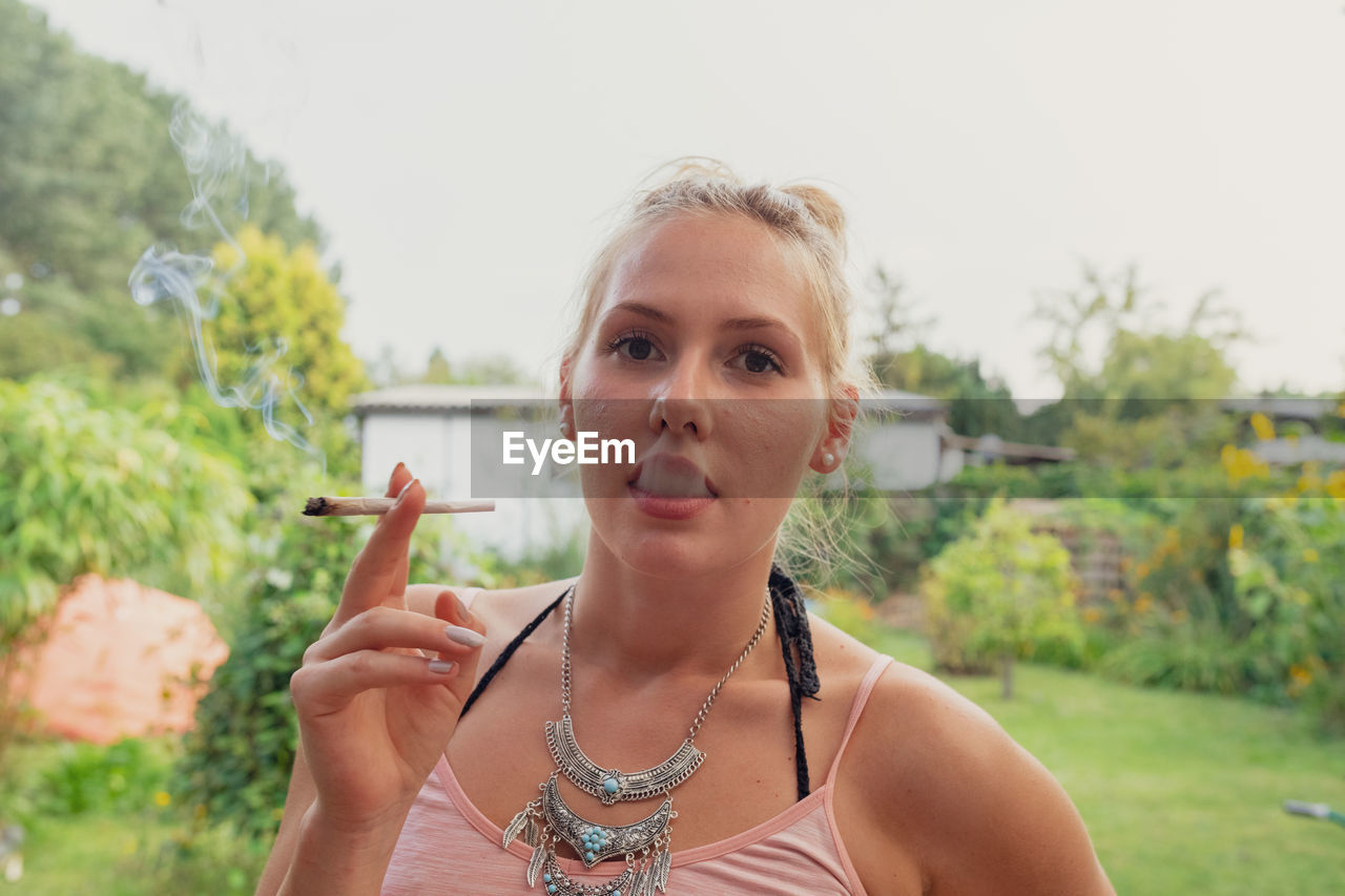 Portrait of young woman smoking marijuana joint while standing outdoors