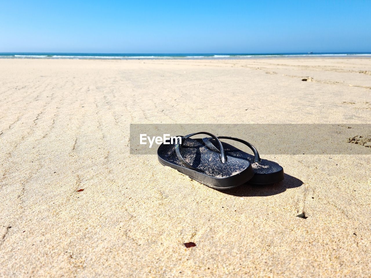 SHOES ON SAND AT BEACH AGAINST SKY
