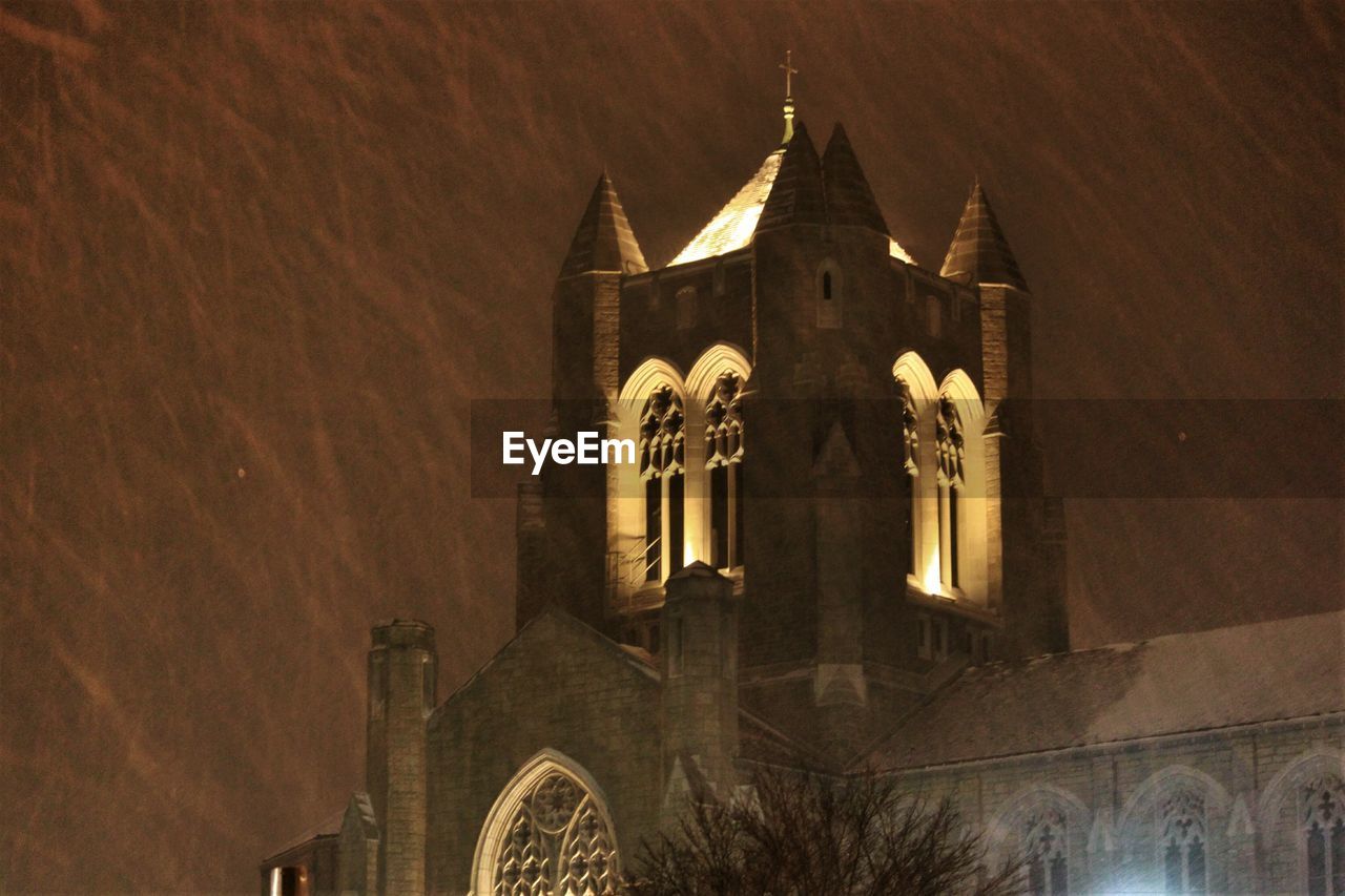 Low angle view of illuminated church against sky during snowfall