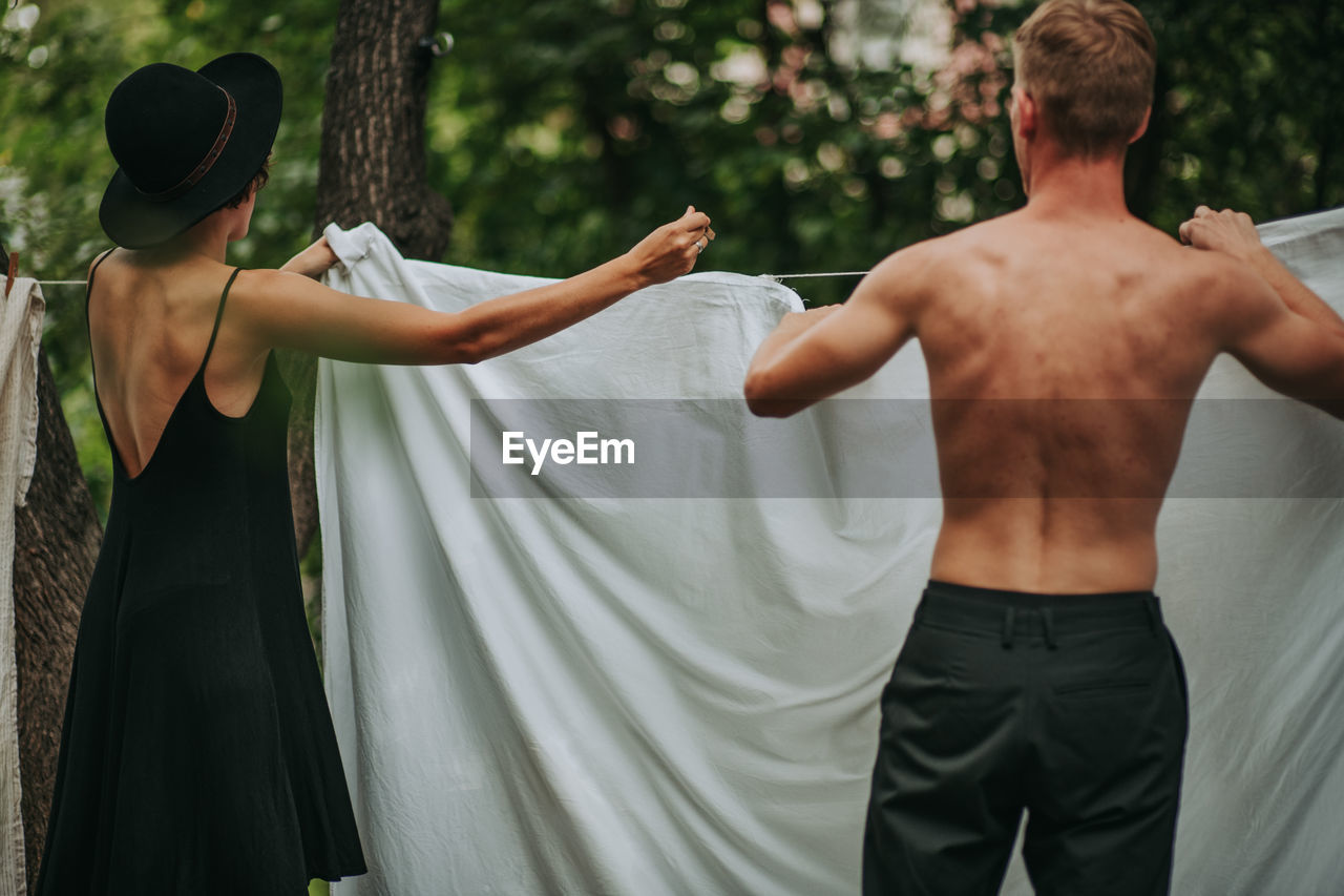 Rear view of shirtless man and woman standing against plants