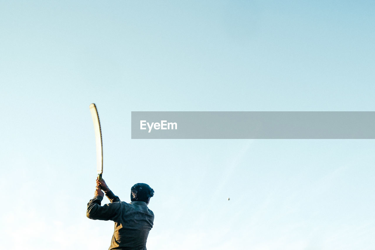 Rear view of man playing cricket while standing against clear sky