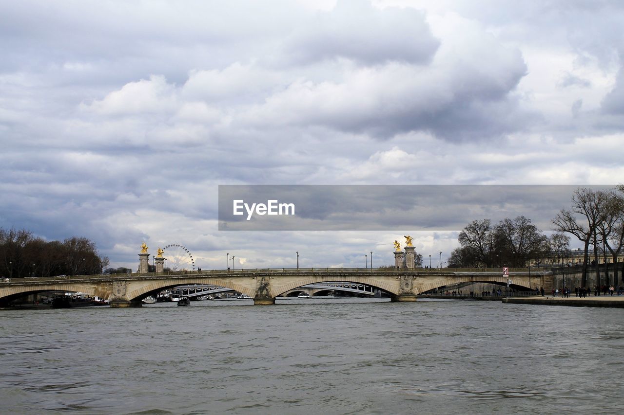 BRIDGE OVER RIVER AGAINST CLOUDY SKY