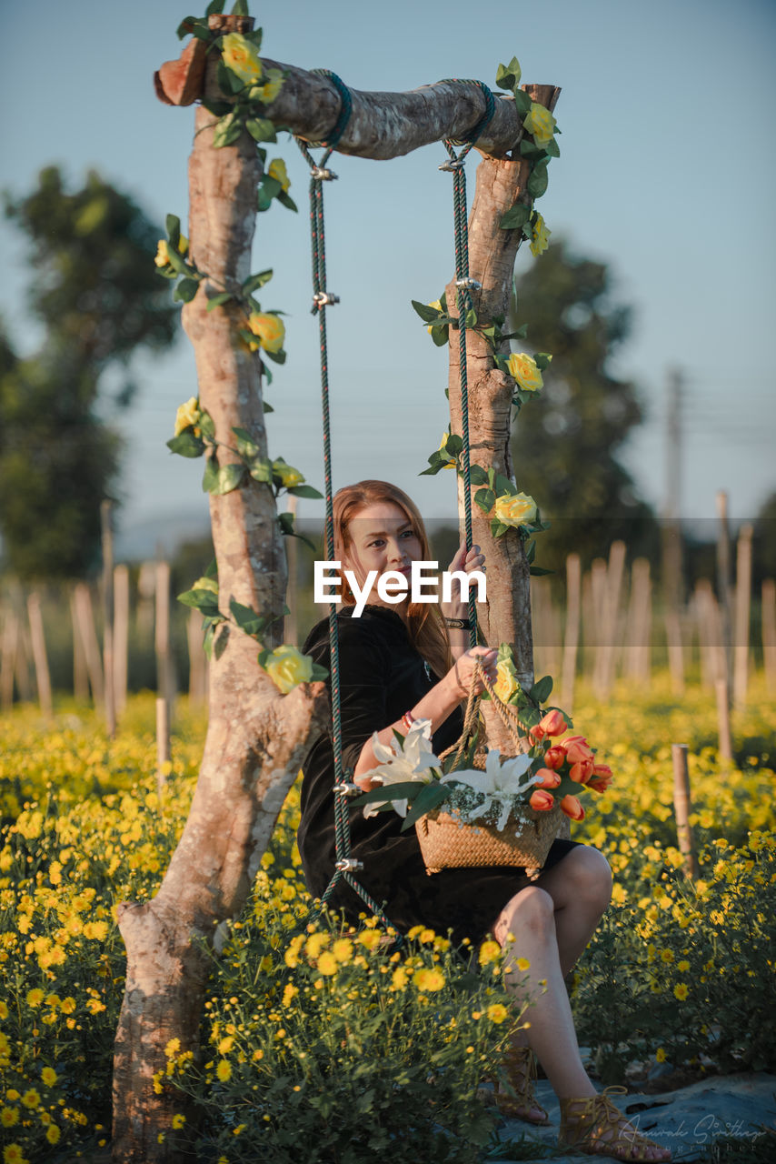 Happy woman holding flowers sitting on rope swing