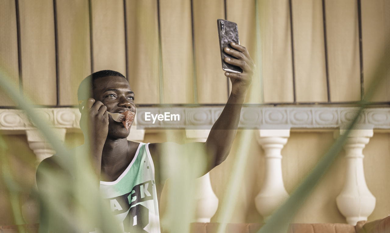 African american eating a piece of fruit and enjoying music on his cell phone while taking a selfie