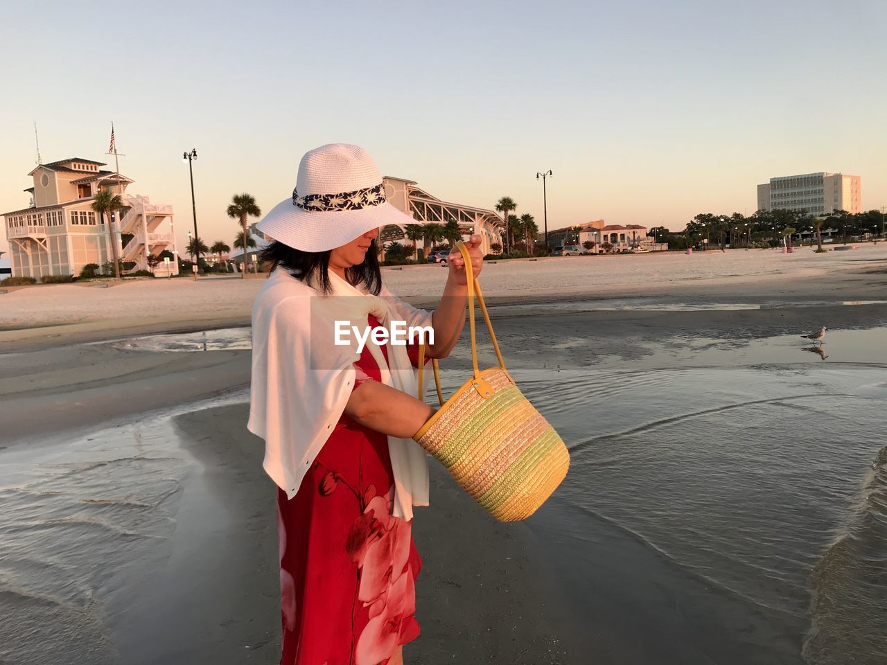 Side view of woman holding shoulder bag while standing at beach sky during sunset