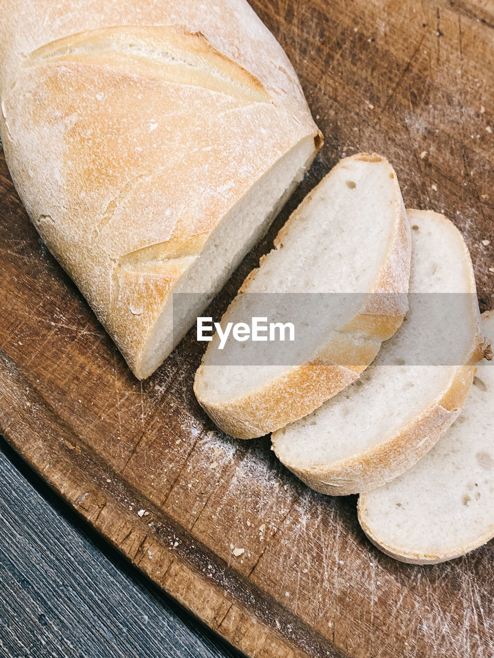 A close up view of a sliced loaf of home made white bread sitting on a dark wooden cutting tray.