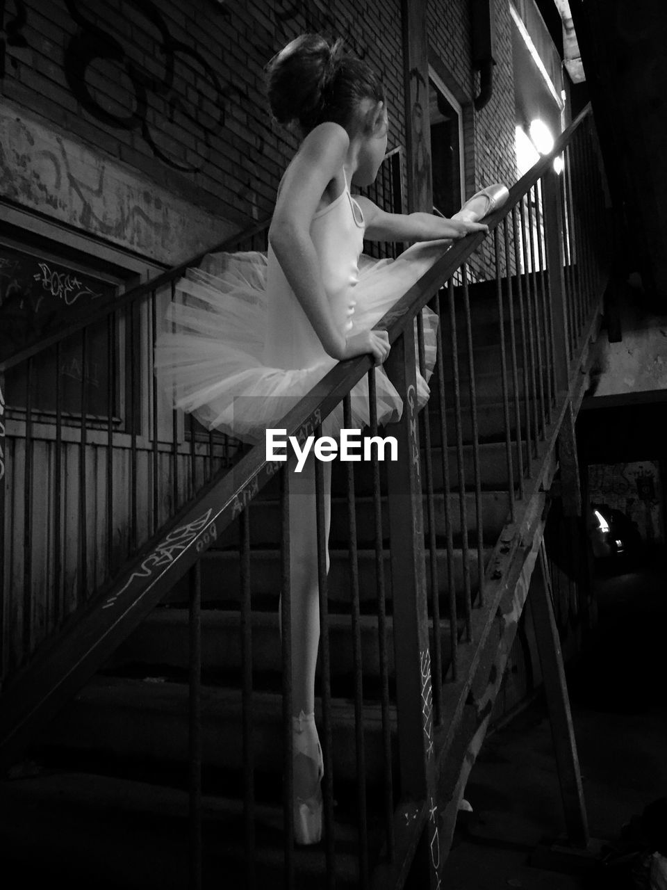 Low angle view of female ballet dancer stretching on steps in abandoned building