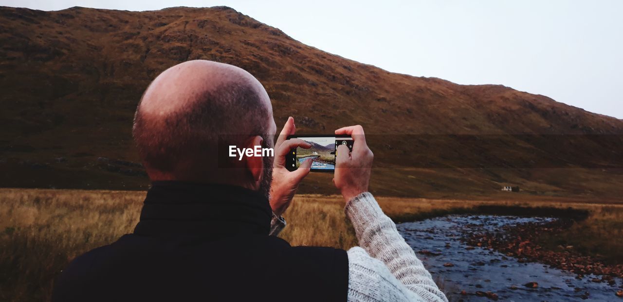 Rear view of man photographing with smart phone