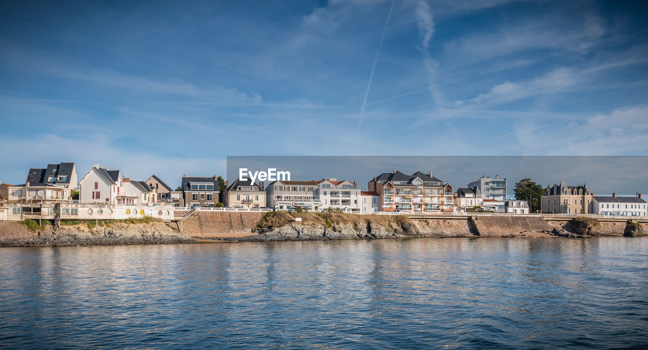 BUILDINGS BY RIVER AGAINST BLUE SKY