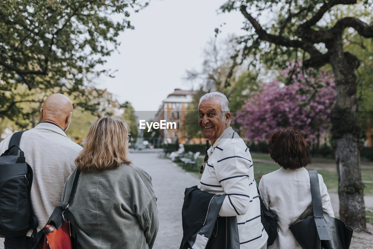 Portrait of smiling senior man looking over shoulder while walking with friends at park