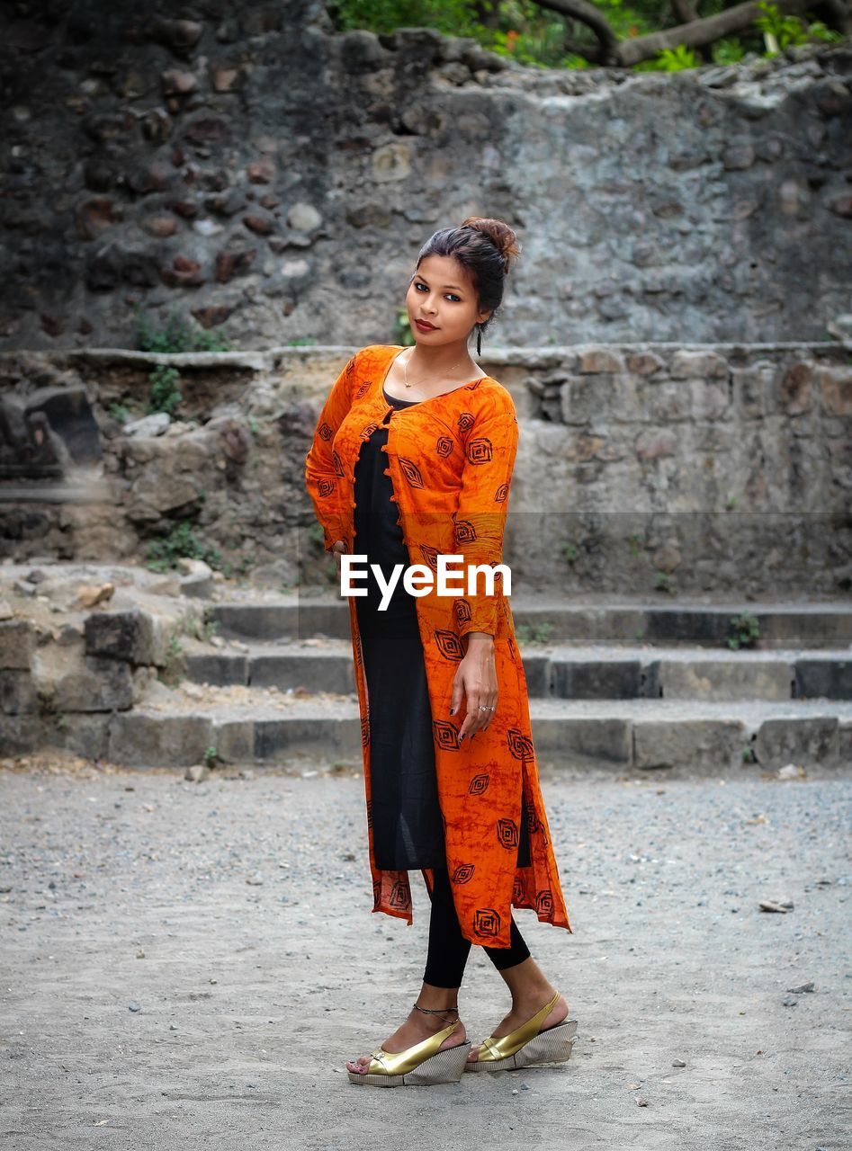 Full length of young woman wearing traditional clothing standing by old wall