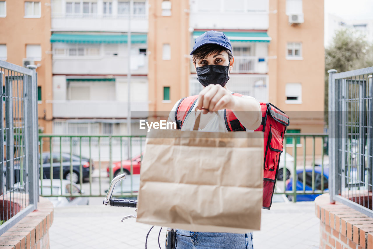 Portrait of delivery person wearing mask giving parcel