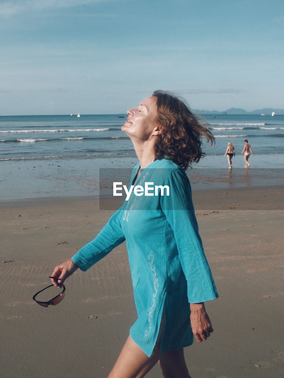 HAPPY WOMAN STANDING ON BEACH AGAINST SEA