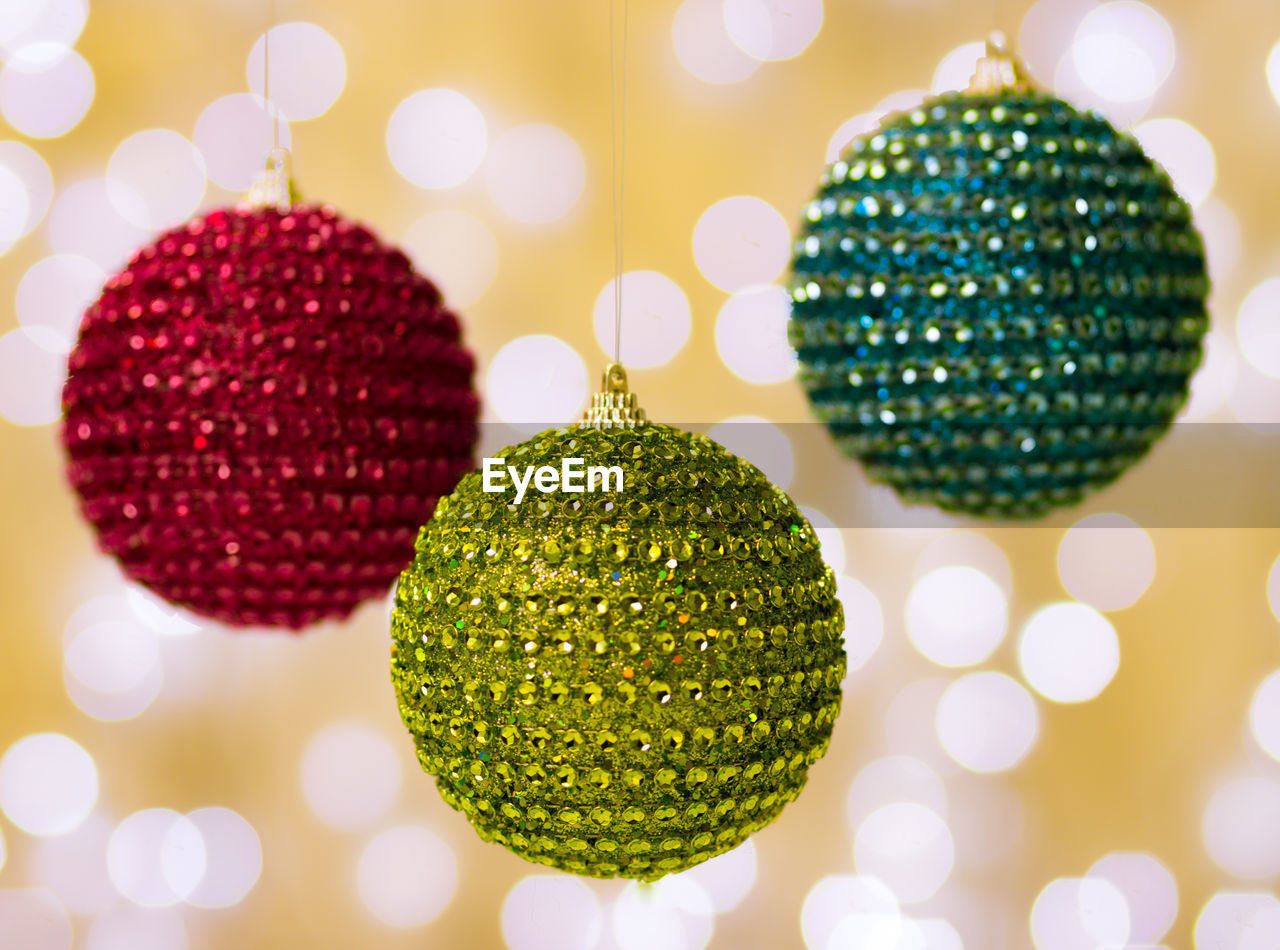 Close-up of christmas ornaments hanging against illuminated light