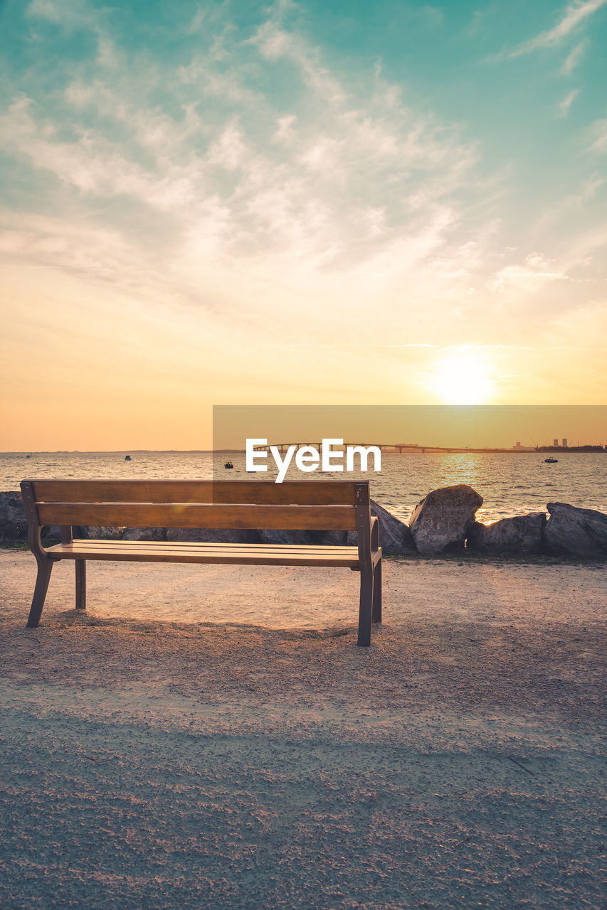 Isolated public bench at sunrise. re island bridge in the background