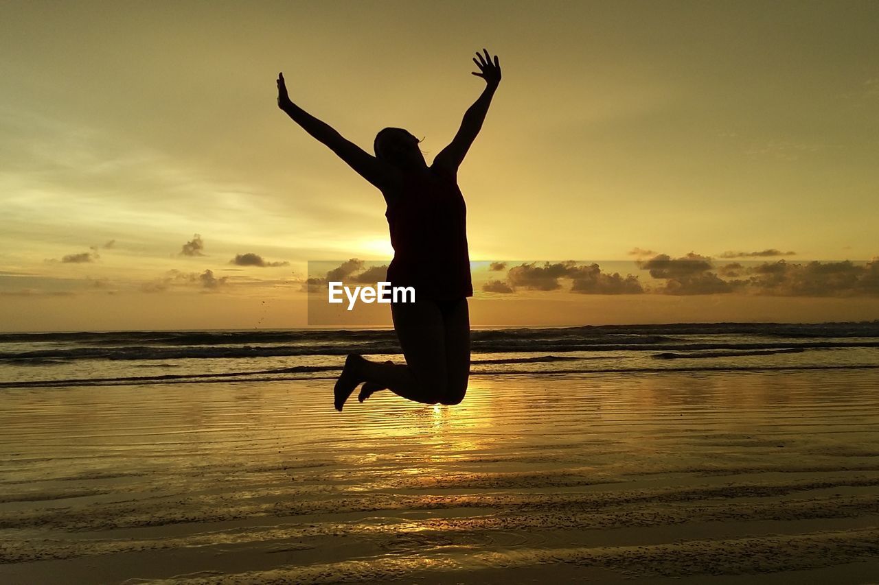 Silhouette woman jumping at beach against sky during sunset