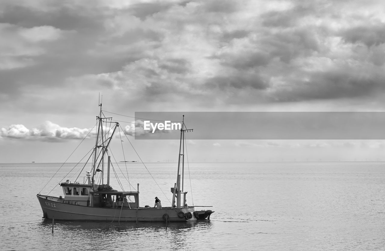 Boats in sea against cloudy sky