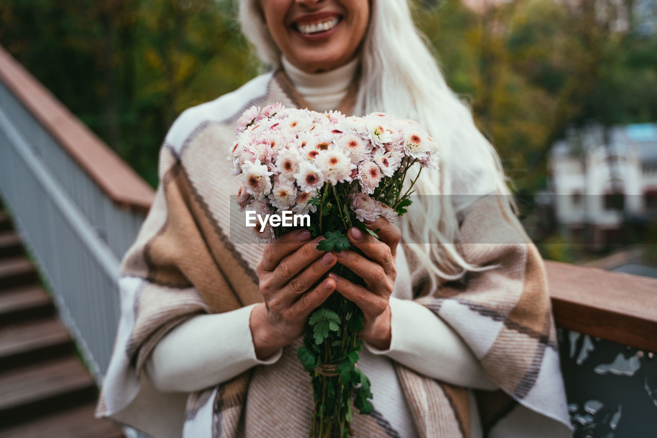 Midsection of woman holding flower bouquet standing outdoors