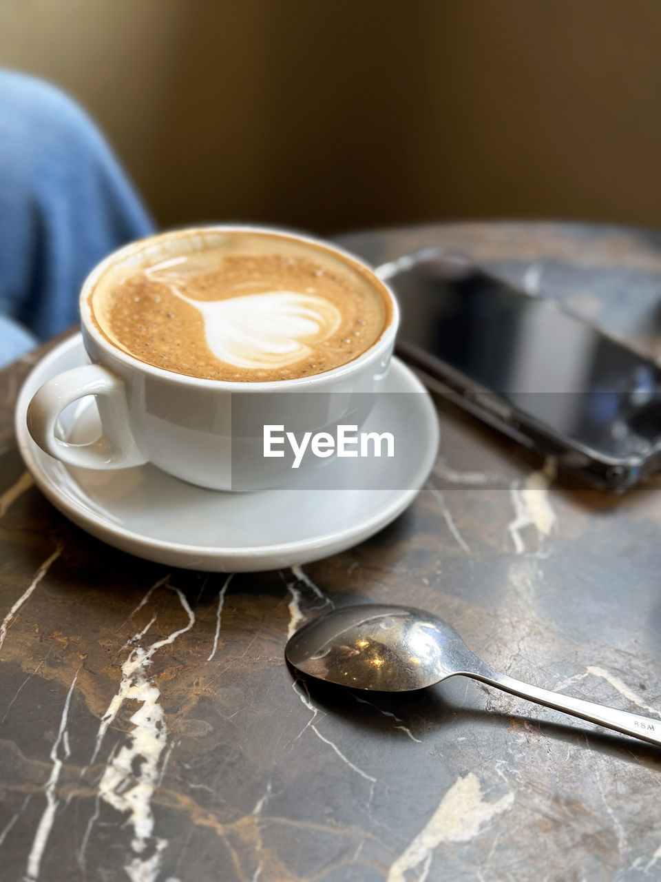 Cappuccino coffee in white cup on marble table with spoon in a cafe.