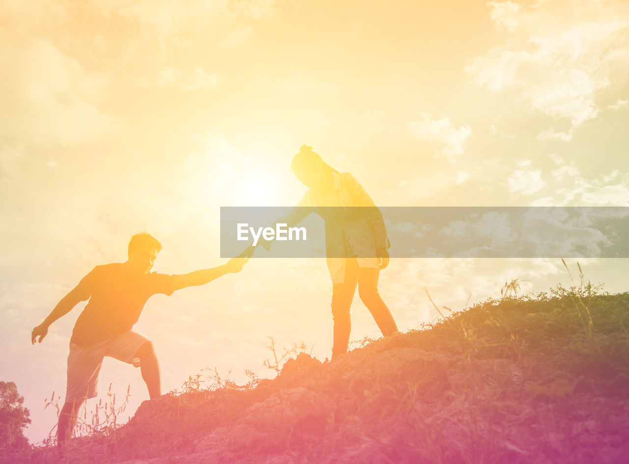 LOW ANGLE VIEW OF FRIENDS STANDING ON LAND DURING SUNSET