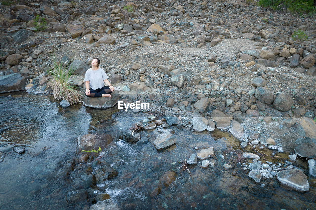 MAN SITTING ON ROCK AT RIVERBANK