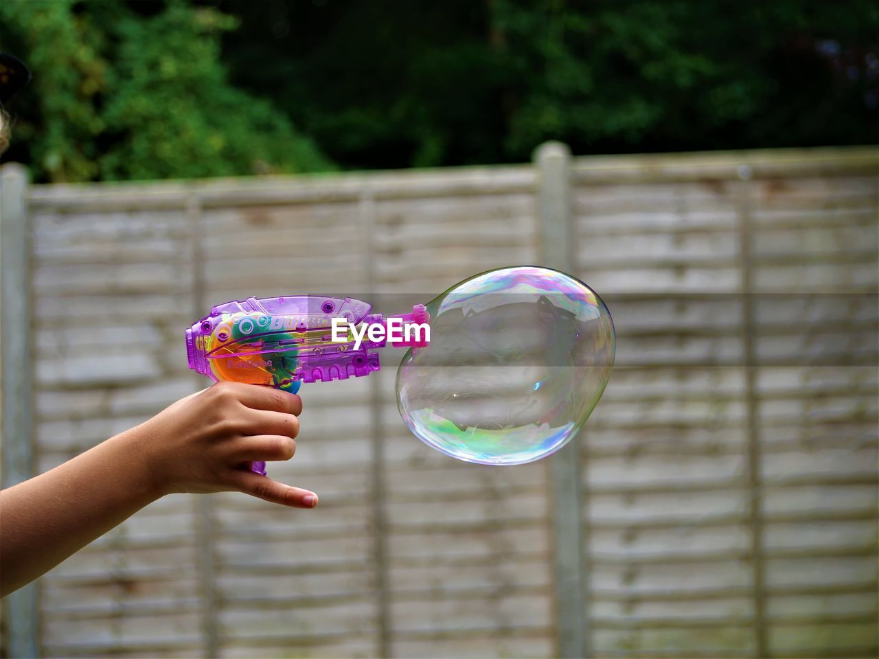 Cropped image of hand holding bubbles against blurred background