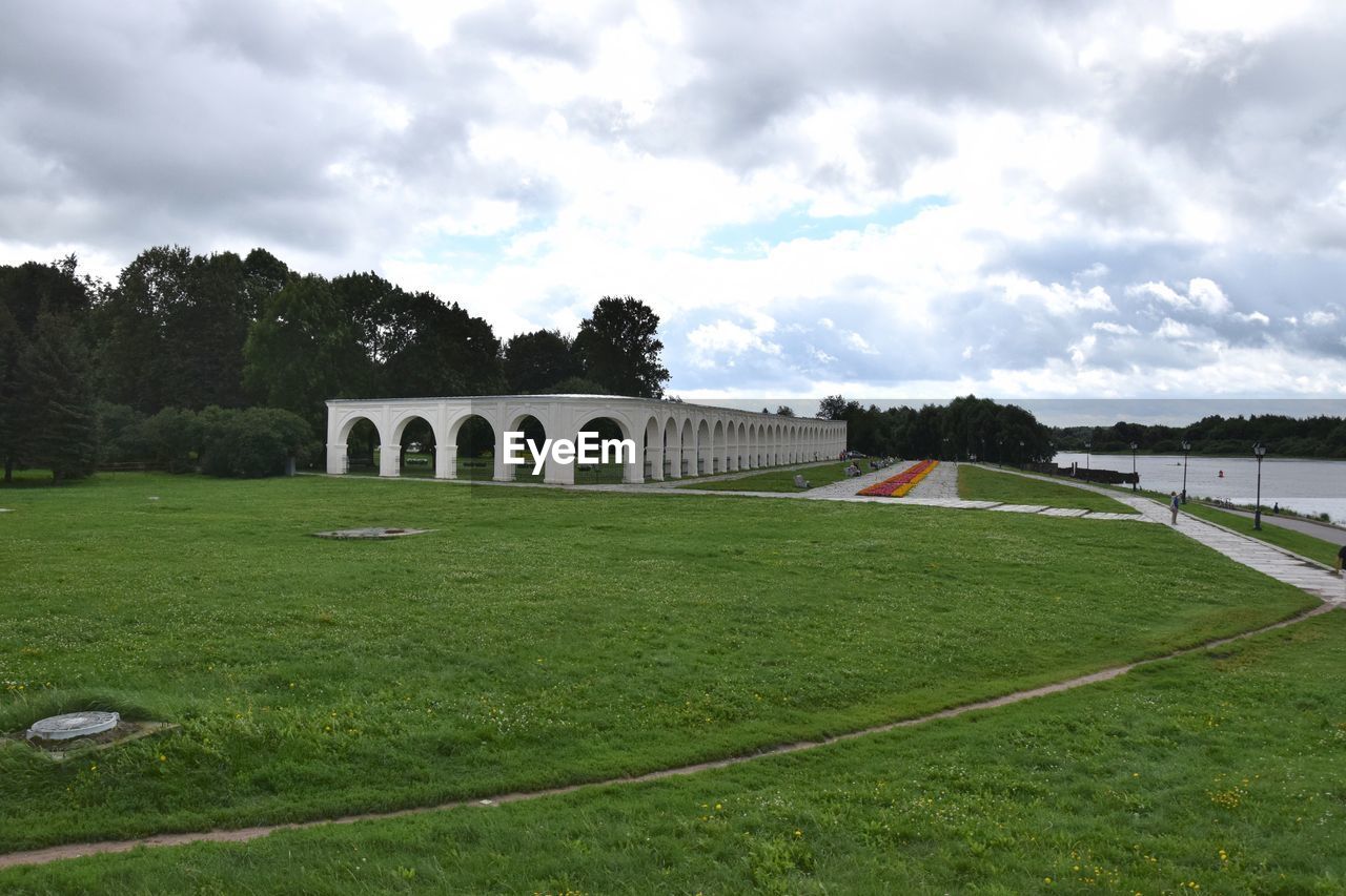 Arch bridge on field against cloudy sky