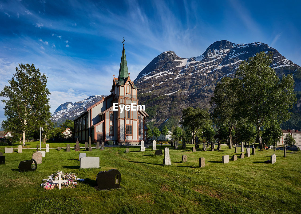 grave, cemetery, tombstone, religion, architecture, grass, stone, sky, plant, place of worship, belief, spirituality, history, the past, built structure, cross, memorial, death, nature, mountain, catholicism, travel destinations, building, building exterior, sadness, no people, landscape, travel, environment, cloud, tree, stone material, scenics - nature, beauty in nature, mountain range, outdoors, grief, tourism, land, green, tranquility, day, field