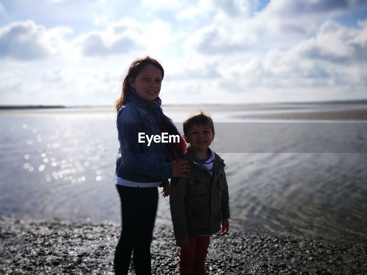 Portrait of smiling siblings standing at beach against sky during sunny day