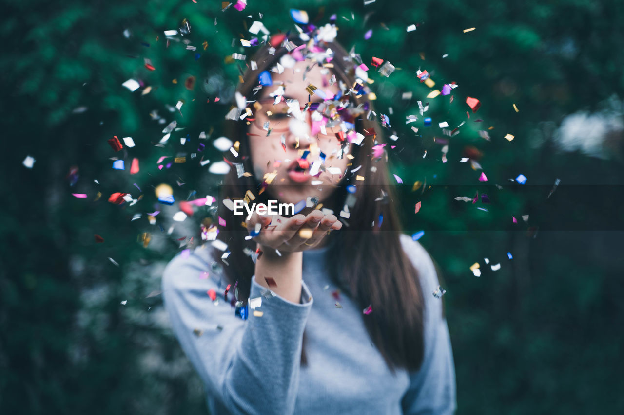 Young woman blowing confetti outdoors