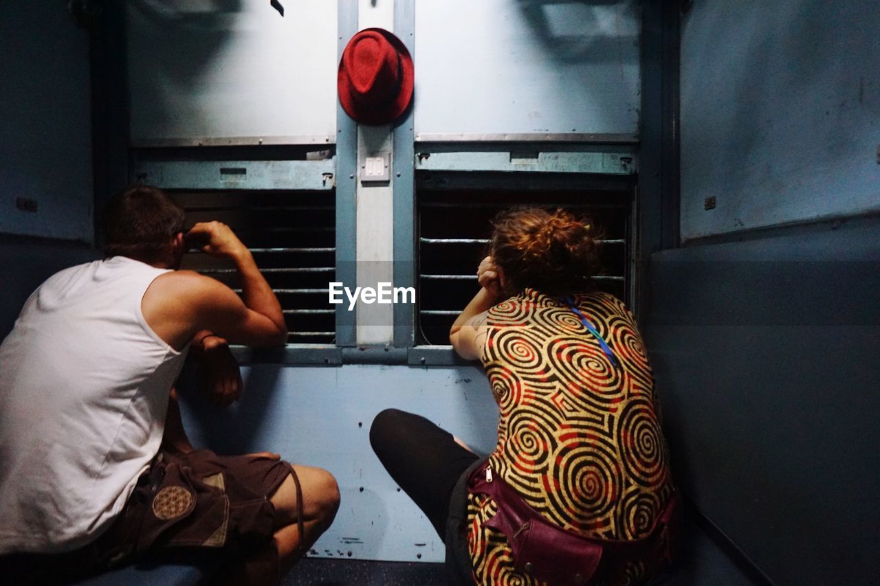 Rear view of people looking through windows in train at night