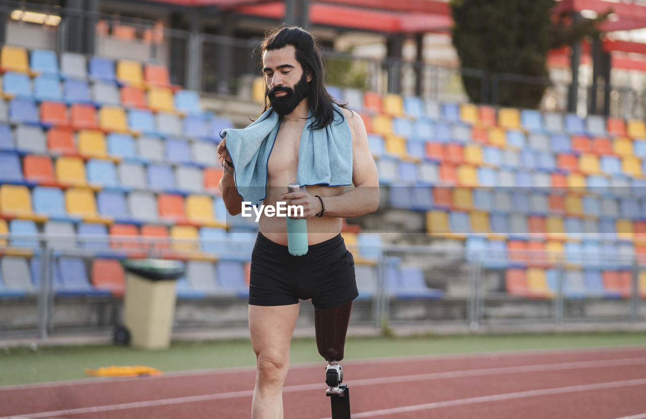 Man with prosthetic leg holding bottle walking on running track