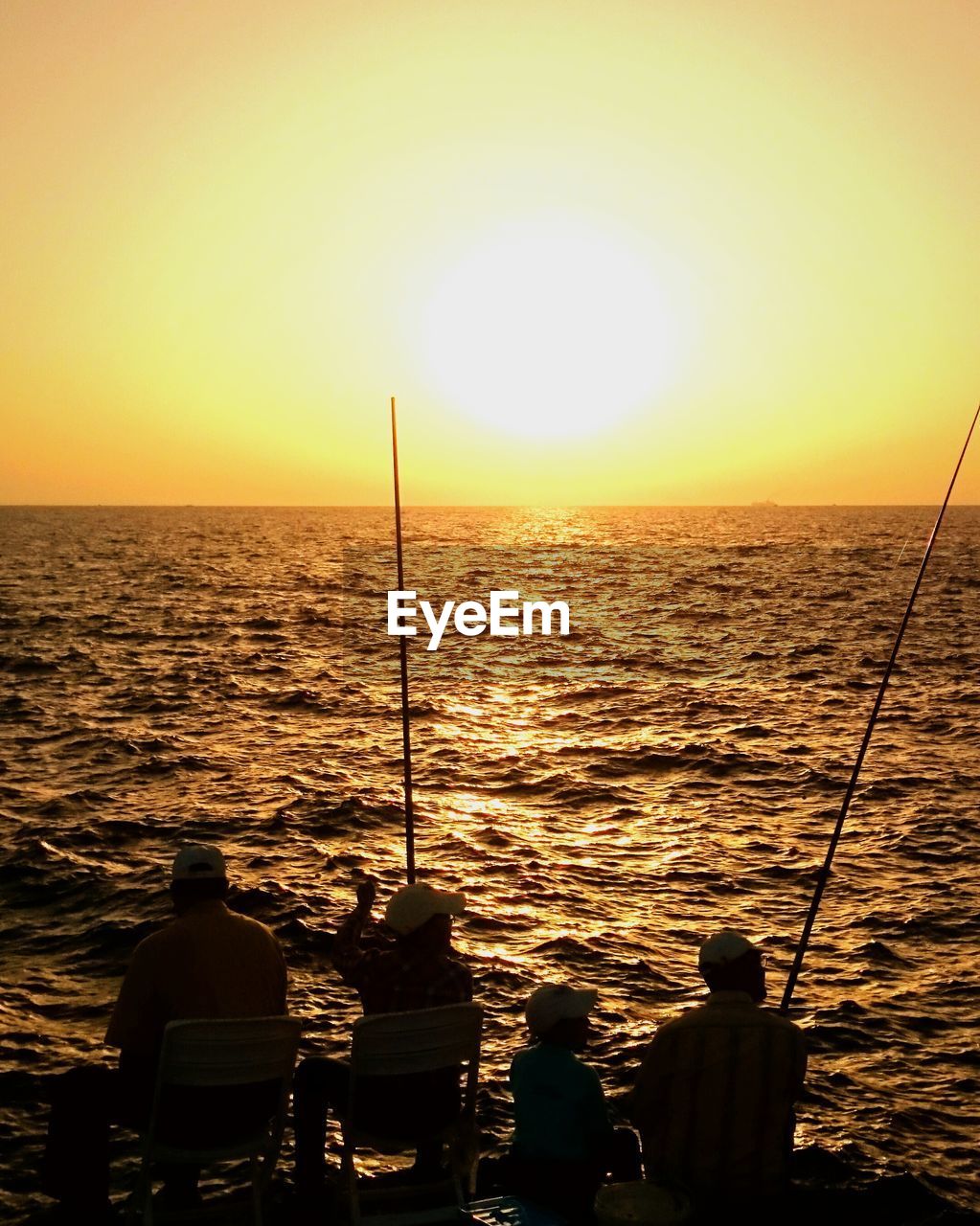 Rear view of silhouette people fishing in sea at sunset