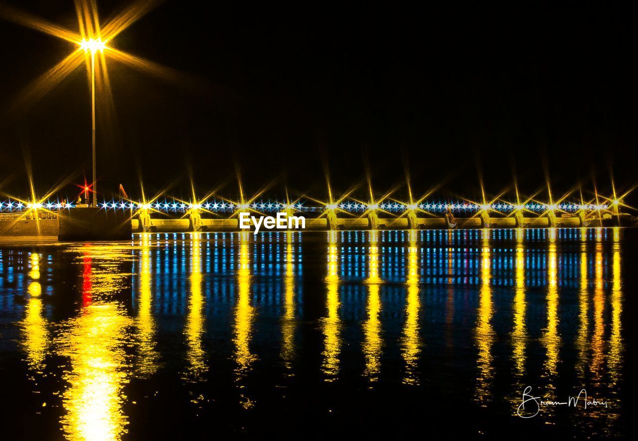 ILLUMINATED BUILT STRUCTURE BY WATER AT NIGHT