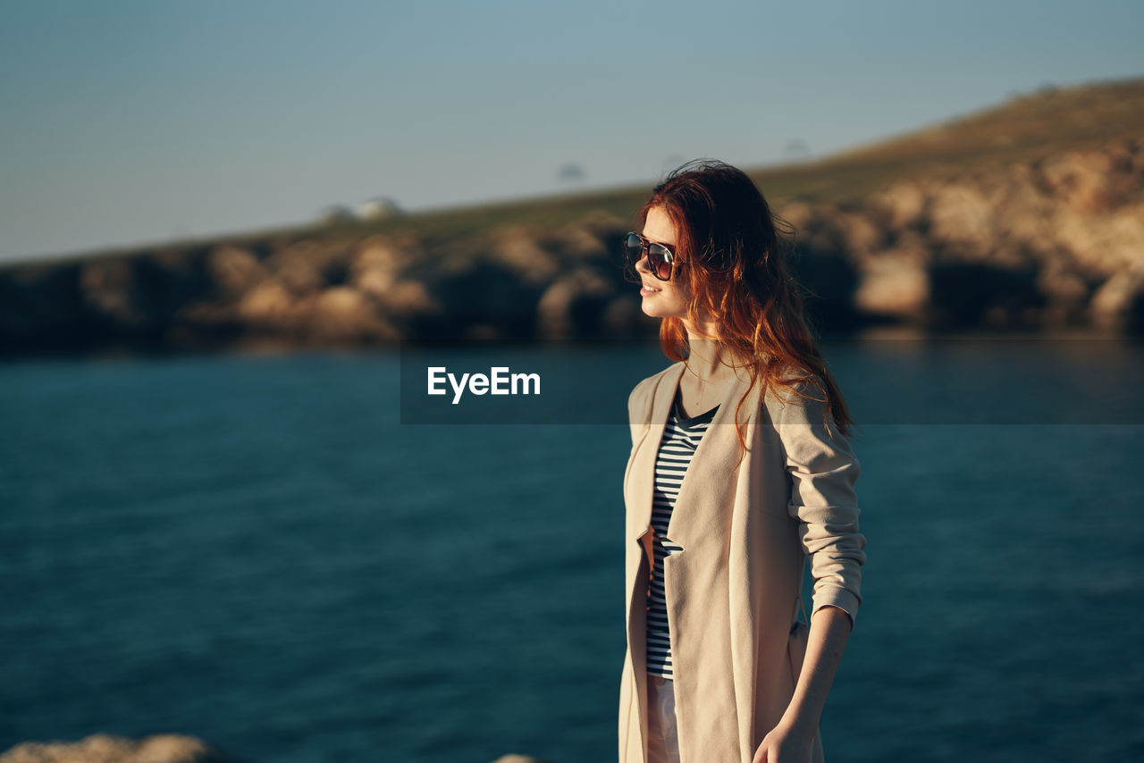 WOMAN WEARING SUNGLASSES STANDING AGAINST SEA
