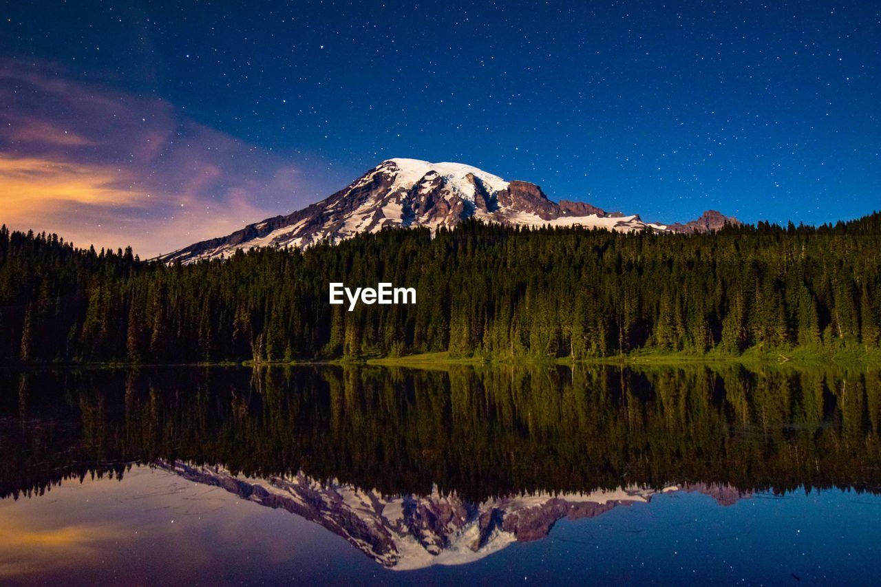 Snowcapped mountain and pine trees against sky reflecting in lake during sunrise at mt rainier national park