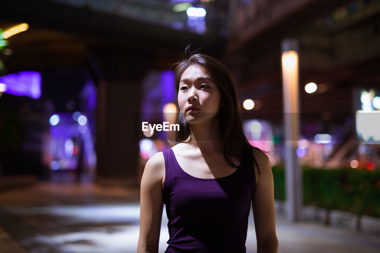 Portrait of smiling woman standing against illuminated city at night