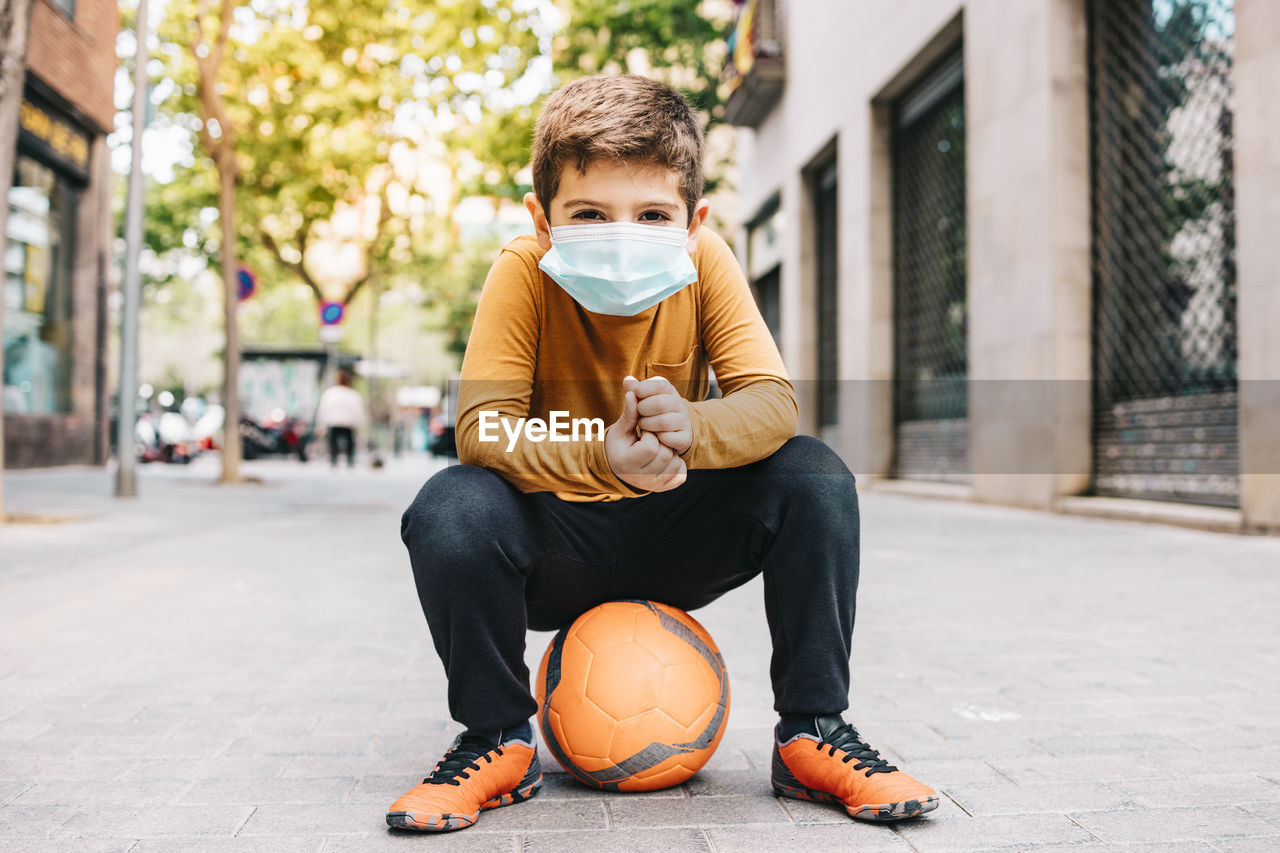 Portrait of boy sitting on sports ball