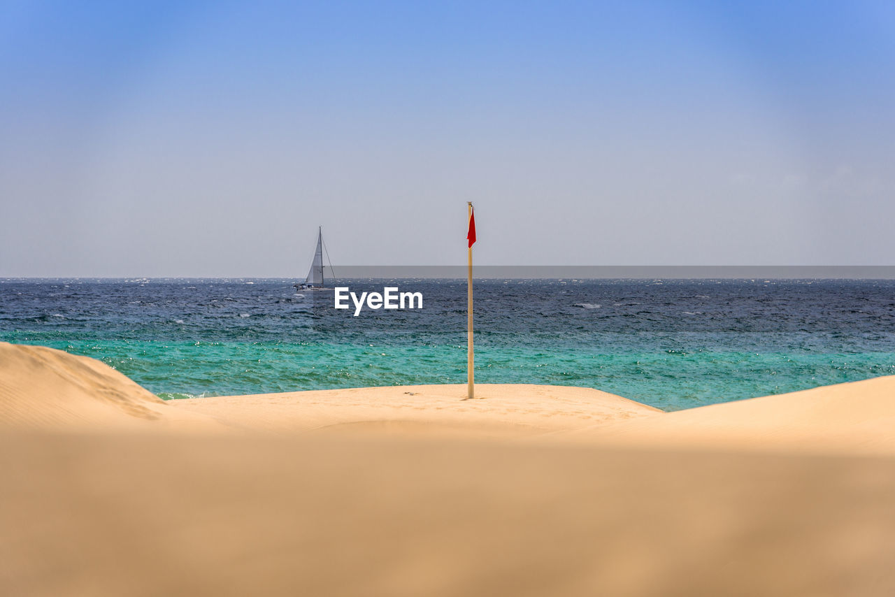 Scenic view of sand and sea against clear sky