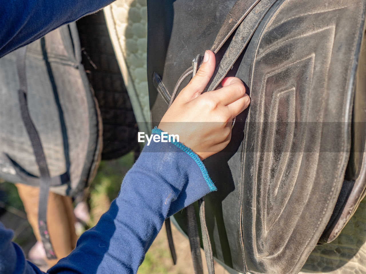 An unrecognizable girl setting horse saddle at horse stable. setting pad and strips of stirrups