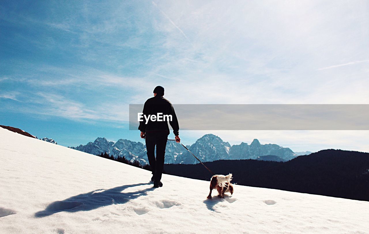 Rear view of man with dog on snow covered mountain against sky