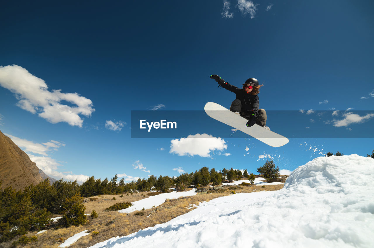 Young woman athlete doing a trick in a jump on a snowboard against a background of blue sky