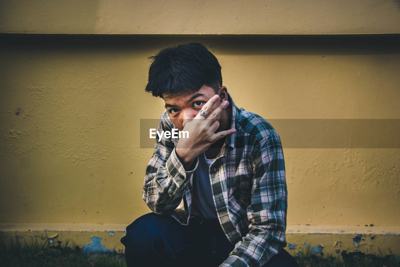 Portrait of young man gesturing against wall