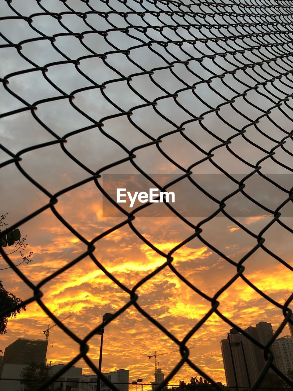 CLOSE-UP OF CHAINLINK FENCE AGAINST SUNSET SKY