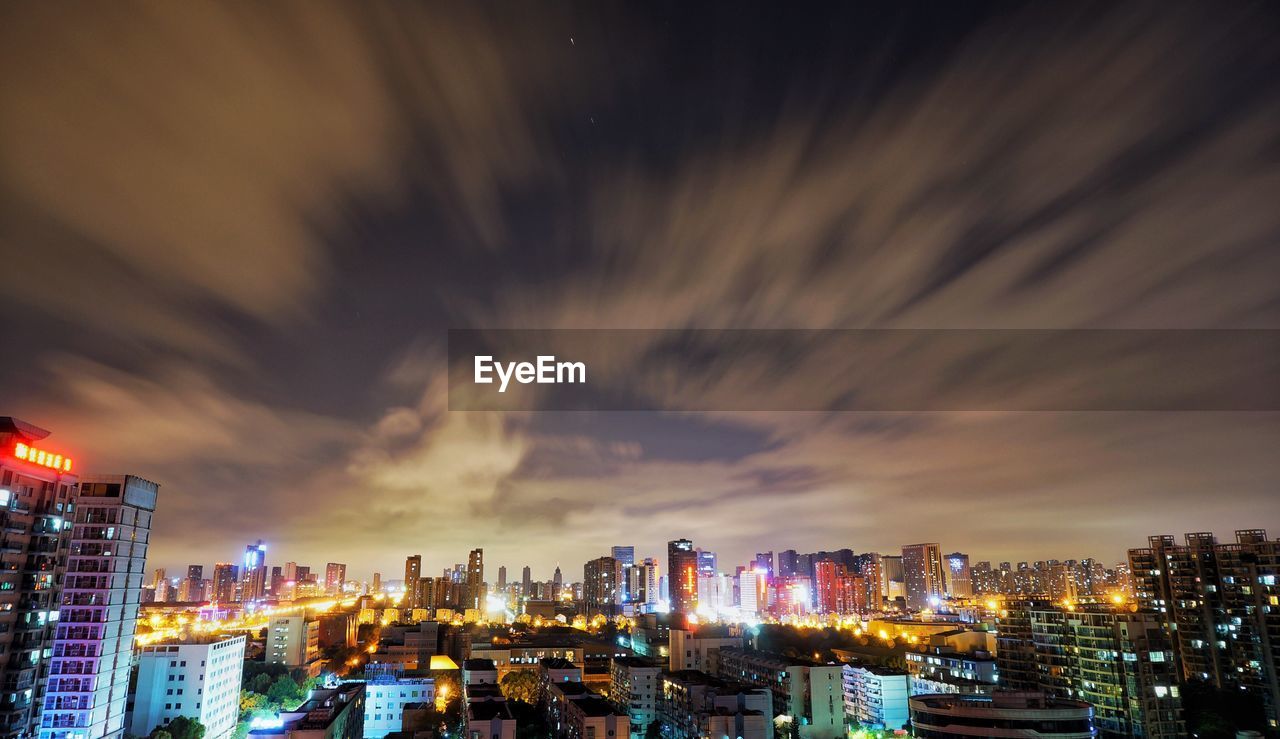 Illuminated cityscape against cloudy sky at night