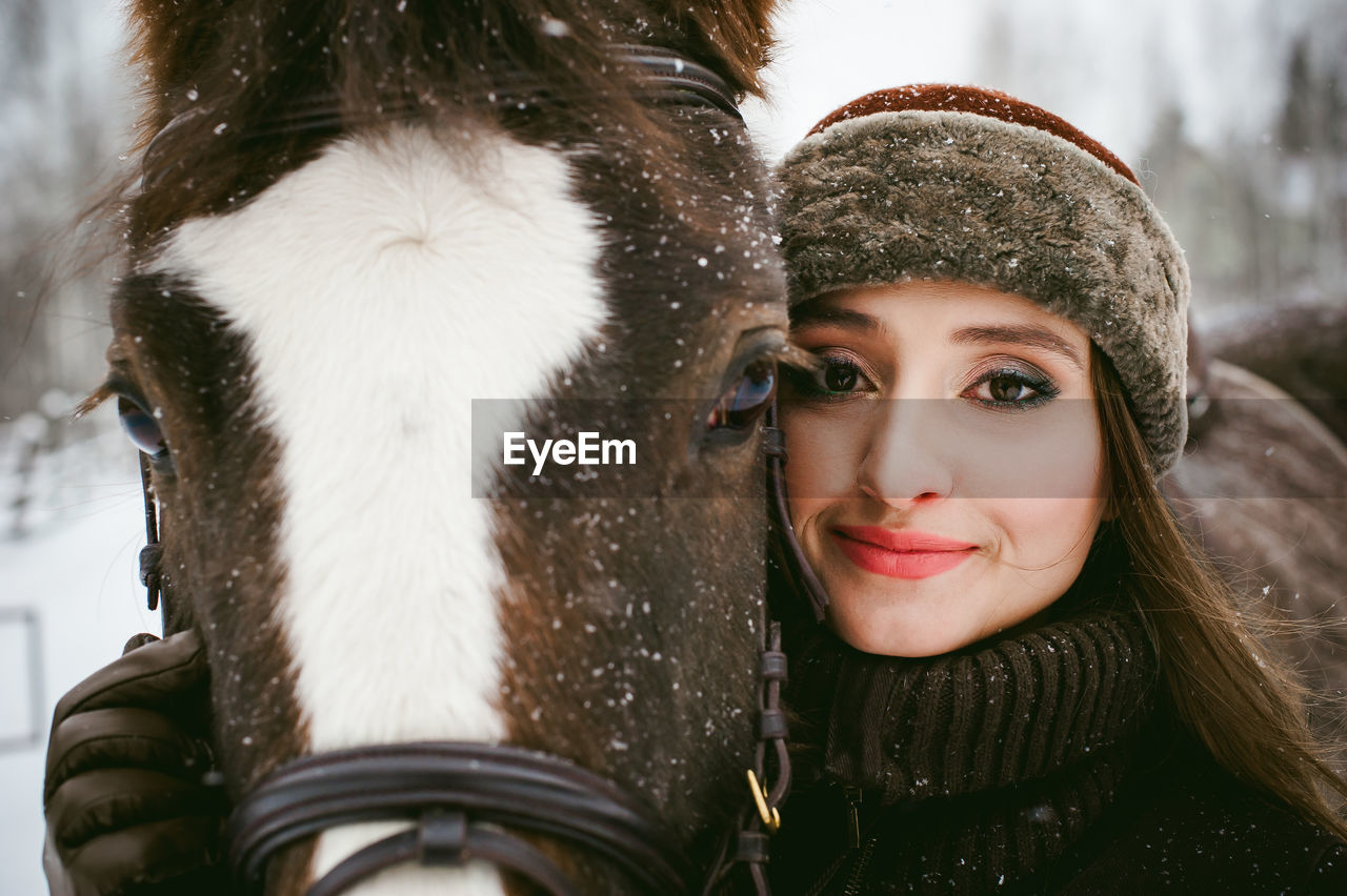 Close-up portrait of beautiful woman with horse during snowfall