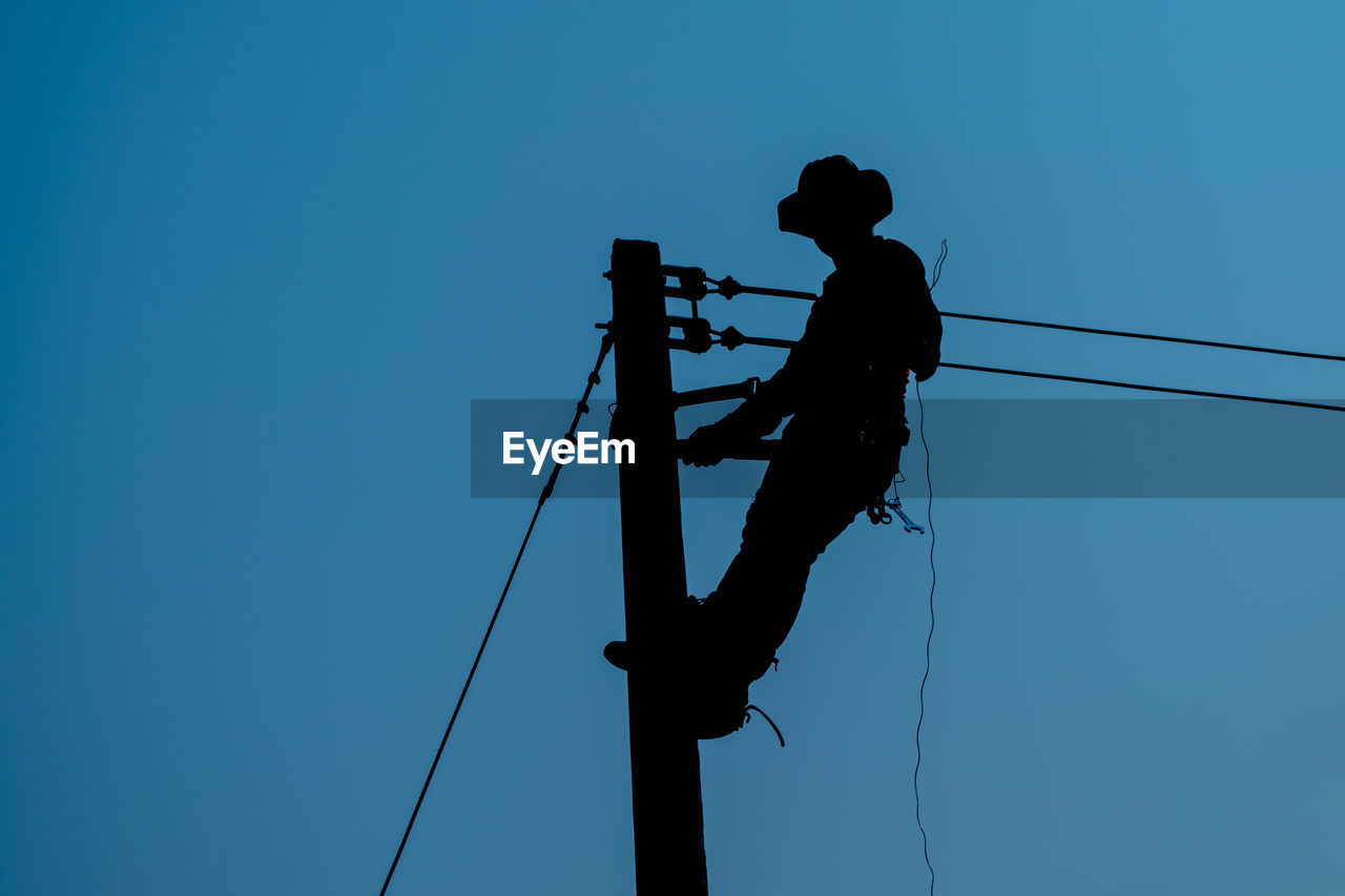 Low angle view of silhouette man against clear blue sky