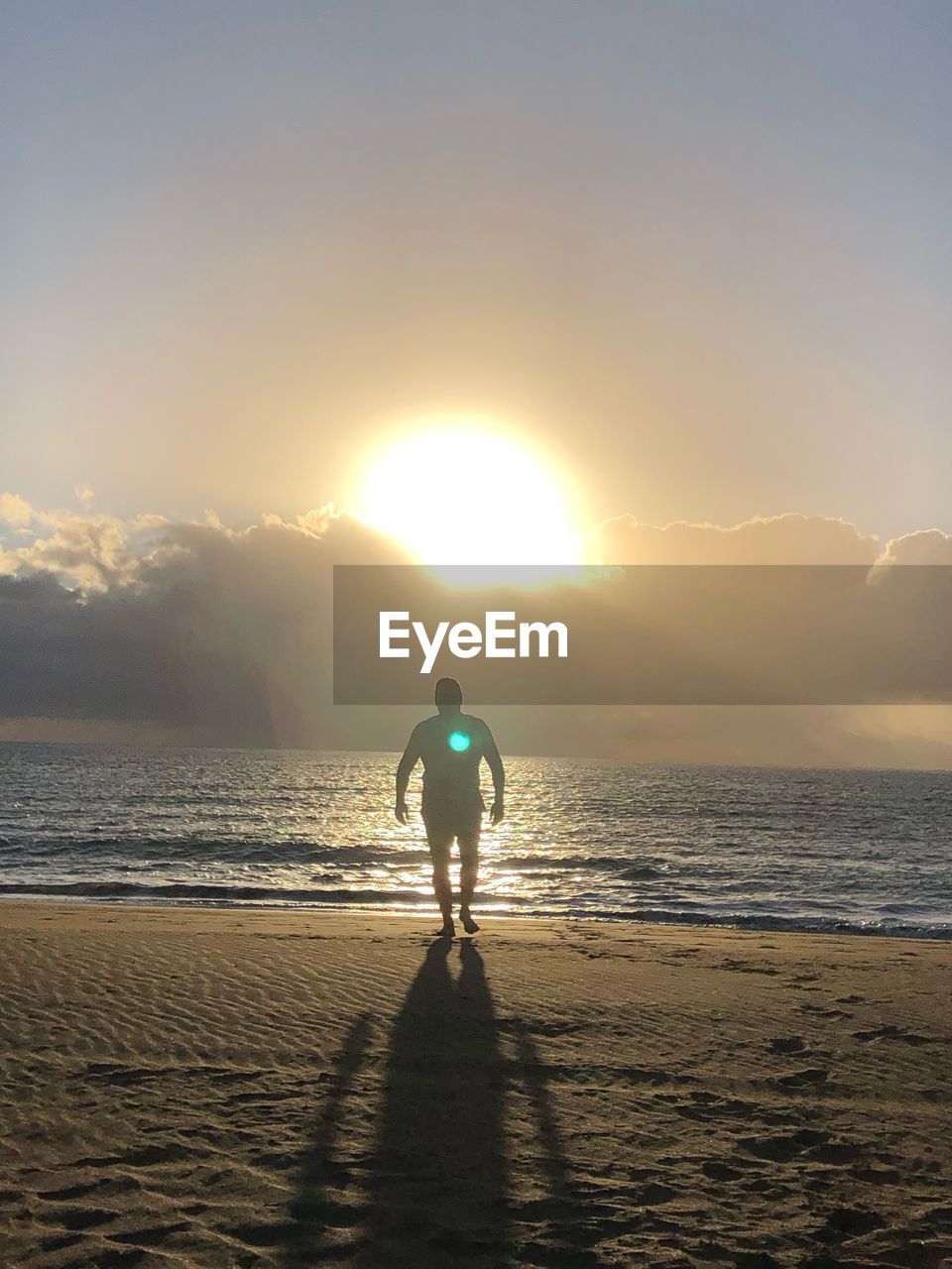 REAR VIEW OF MAN ON BEACH DURING SUNSET